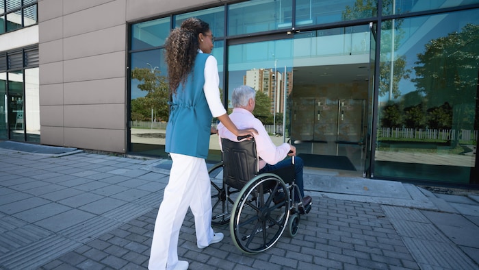 Une jeune femme noire ramène chez lui un homme âgé en fauteuil roulant.