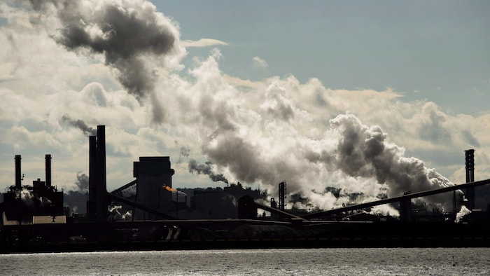 Une usine sur le bord de l'eau. De grandes volutes de fumée s'échappent et assombrissent le ciel.