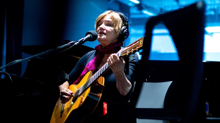 Diane Tell en train de chanter et de jouer de la guitare en studio.