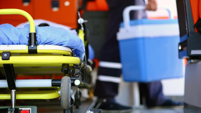 Un ambulancier porte une glacière bleue pour un don d'organes. Une civière se trouve à l'avant-plan.