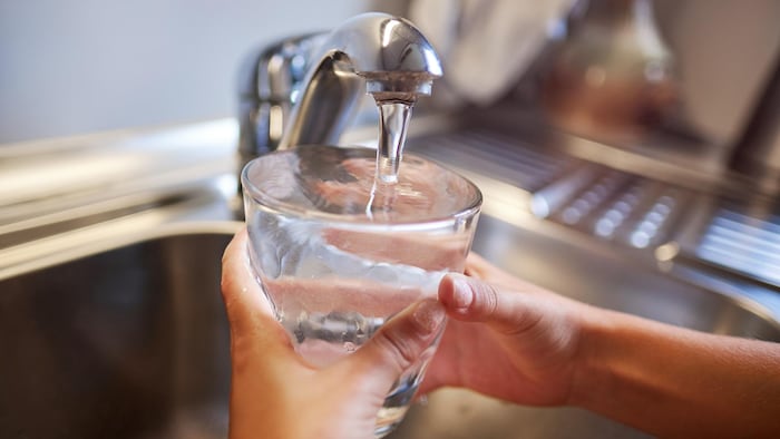 Des mains tiennent un verre rempli d'eau sous un robinet de cuisine. 
