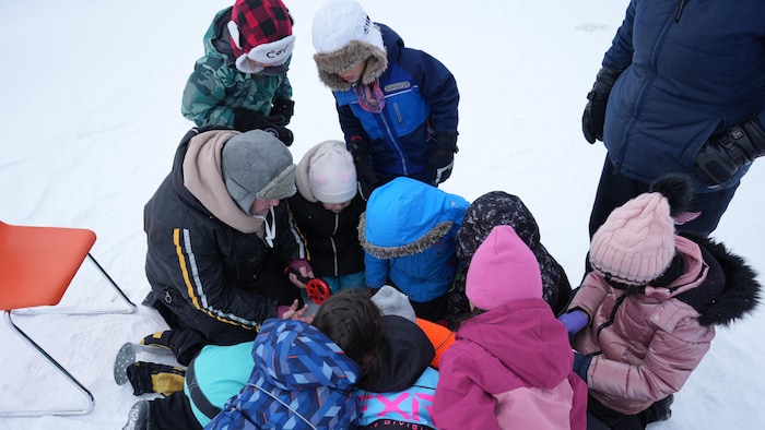 Les élèves de la deuxième année sont regroupés autour d'une enseignante qui leur montre comment pêcher sur la glace.