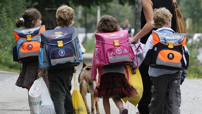 Des écoliers se rendent à l'école; chacun porte un sac à dos. 