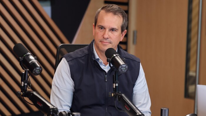 Éric Sansoucy assis derrière un micro, dans un studio de radio.
