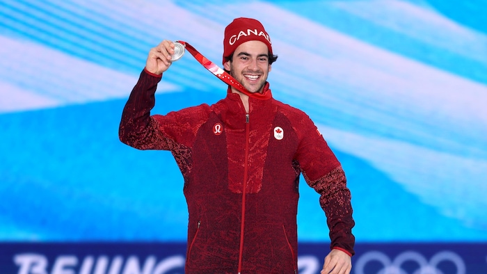 Éliot Grondin, souriant, tient sa médaille haut dans les airs.
