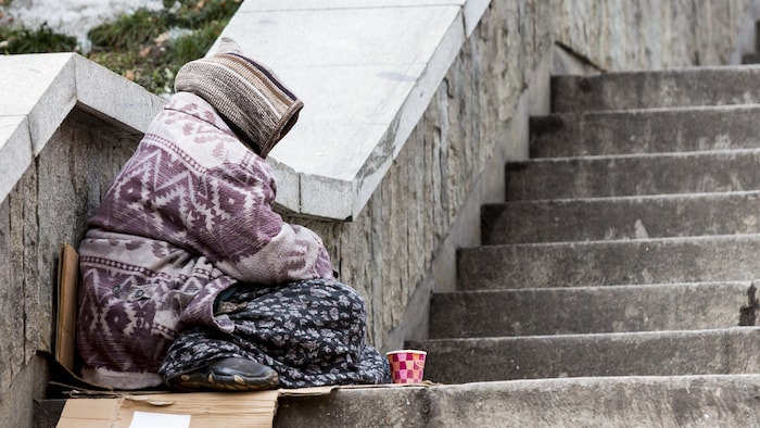 Profil d'une femme emmitouflée dans ses vêtements et assise dans un escalier.