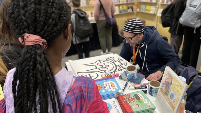 Un dessinateur lors d'un salon du livre face à un public d'enfants.