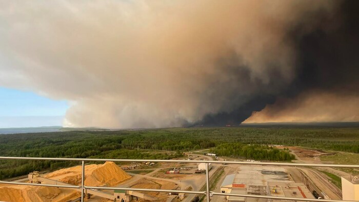 Un incendie de forêt brûle à l'horizon non loin du site d'une usine qui transforme du bois en pâte à papier.
