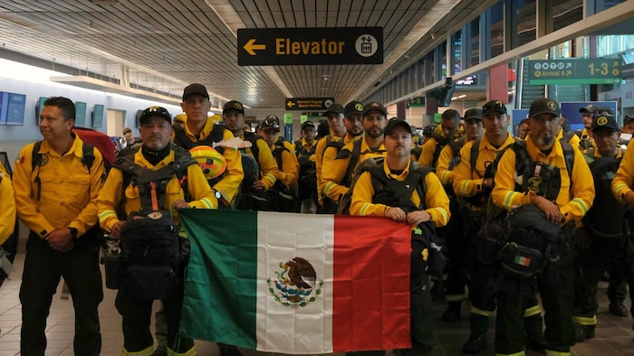 Plusieurs pompiers, dans leurs uniformes et tenant un drapeau du Mexique.