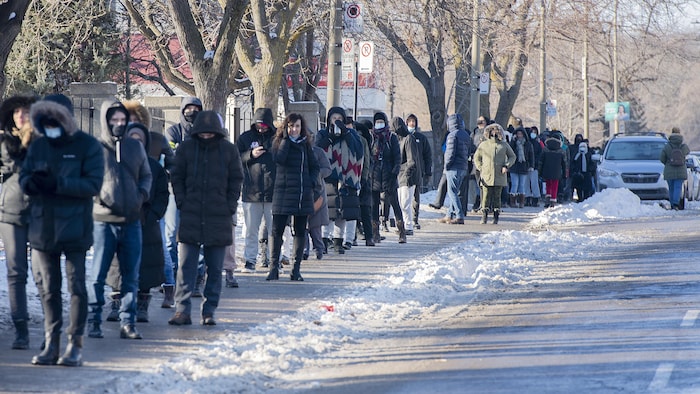 Des gens chaudement vêtus sont en ligne sur le trottoir, un jour d'hiver.