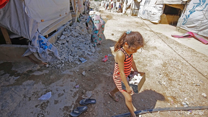 طفلة تحمل صندوقاً يحوي قطعاً صغيرة من الإسمنت في مخيم للاجئين.