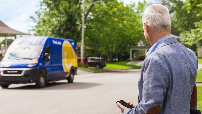 Un homme muni d'un téléphone intelligent attend un véhicule de transport en commun.