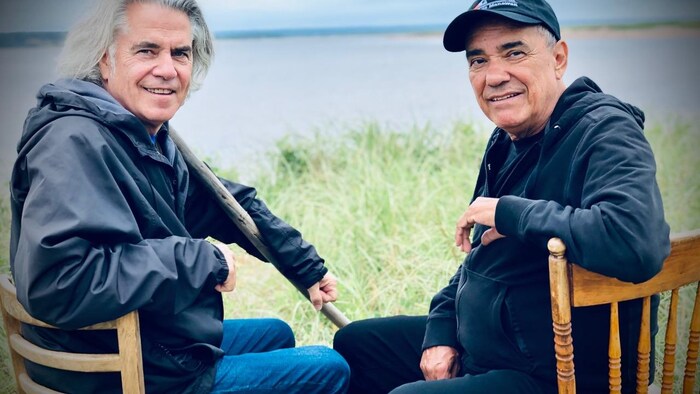 Richard Séguin et Florent Vollant posent ensemble sur des chaises près de l'eau.