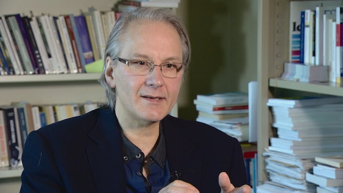 Le politologue Frédéric Boily dans son bureau, avec des bibliothèques remplies de livres derrière lui.