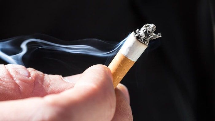 Une main tient un mégot de cigarette allumée.