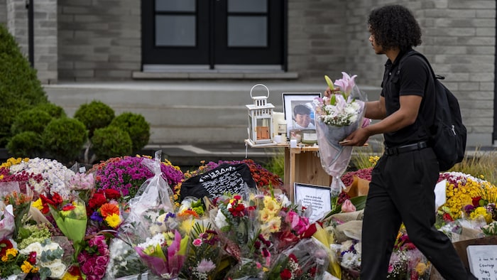 Un adolescent apporte un bouquet de fleurs à un mémorial devant une maison de banlieue.
