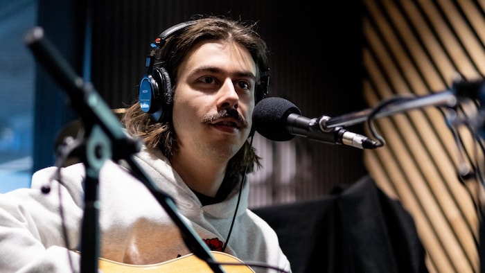 L'artiste est assis avec des micros devant lui avant qu'il n'effectue une prestation en direct, accompagné de sa guitare.