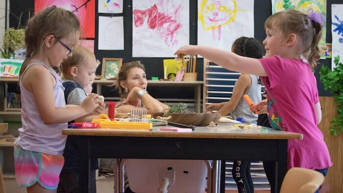 Des enfants jouent avec leur éducatrice à une table.