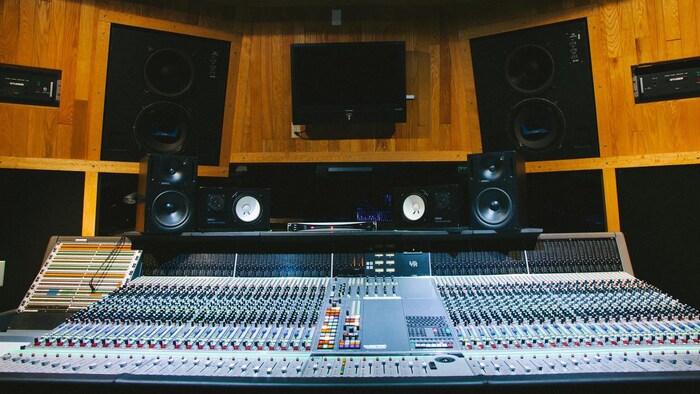 Vue d'une grande console audio dans une salle de mixage son en bois.