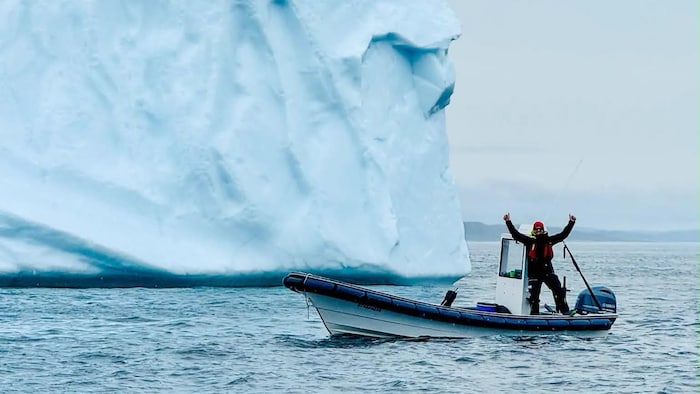 Un homme en chalouppe près d'un iceberg