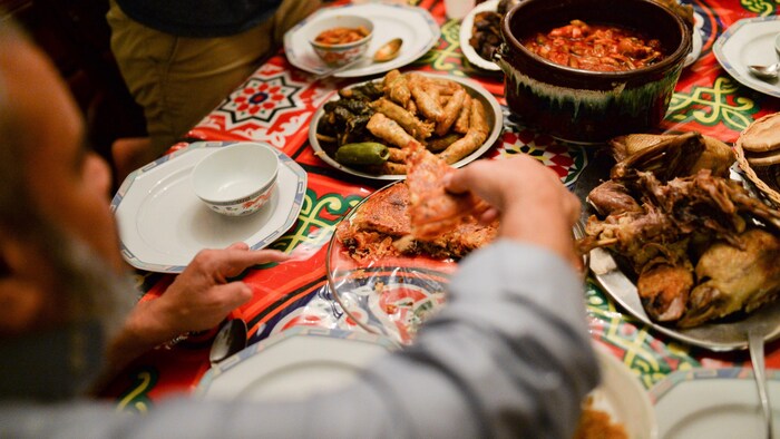Une main d'homme se sert de la nourriture parmi plusieurs plats disposés sur une table colorée.