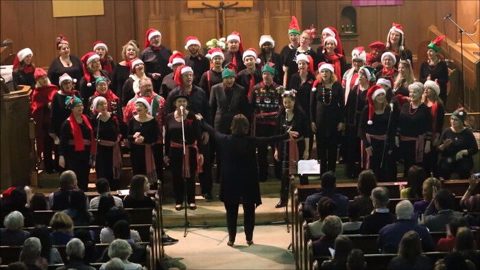 Dans une église, le chœur Les Voix du cœur et plus d’une trentaine de choristes, qui portent des chapeaux de lutins de Noël.