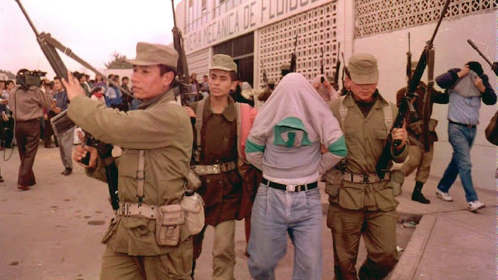 Des soldats  escortent deux hommes qui cachent leur visage.