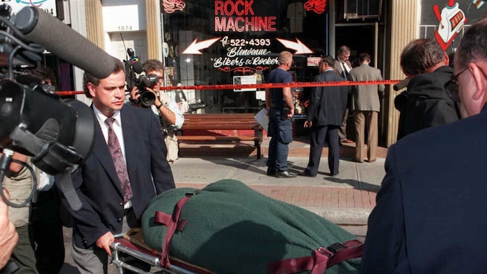 Des hommes transportent le corps d'un motard devant un commerce d'accessoires des Rock Machine.