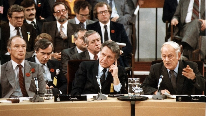 Pierre Elliott Trudeau, Allan MacEachen écoutent René Lévesque qui parle dans un micro.