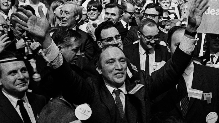 Surrounded by a crowd, Pierre Elliott Trudeau raises his hands in victory.