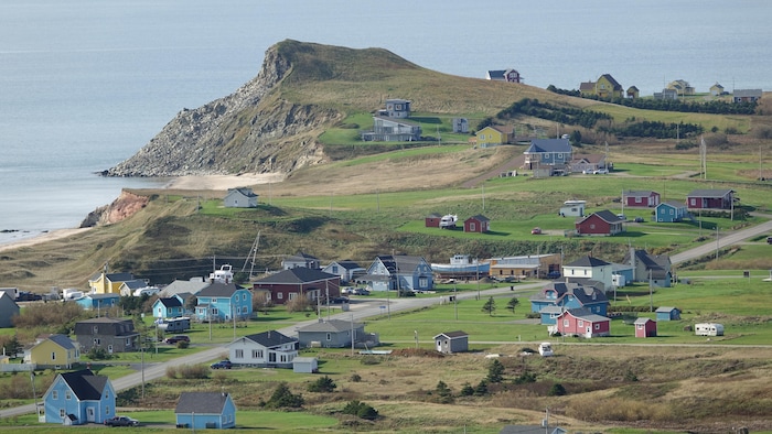 Un paysage rural avec des maisons colorées et une butte rocheuse à l'arrière-plan.