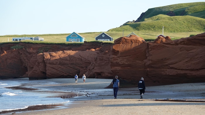 Des gens marchent sur la plage de la Dune-du-Sud, au pied de falaises de grès rouge.