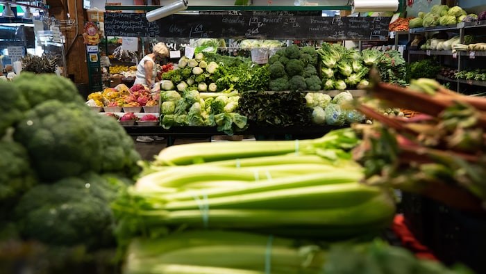 Une personne fait ses courses dans le rayon légumes frais dans un marché.