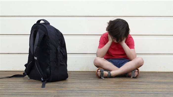 Un enfant se prenant la tête, assis avec son sac d'école.