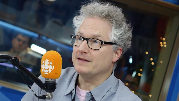 Un homme aux cheveux blancs discute devant un micro au studio 17 de Radio-Canada. 