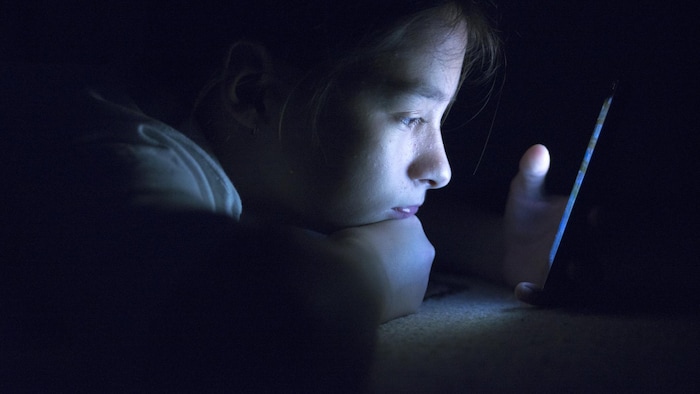 Un jeune dans le noir tient son téléphone très près de son visage.