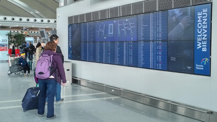 مسافران ينظران إلى لوحة المغادرة والوصول في مطار بيرسون الدولي في تورونتو.