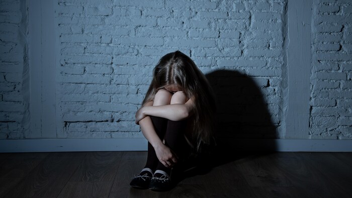 Une jeune fille recroquevillée contre un mur.
