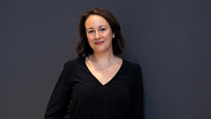 Portrait de Karine Godin appuyée contre un mur et souriant à l'appareil photo.