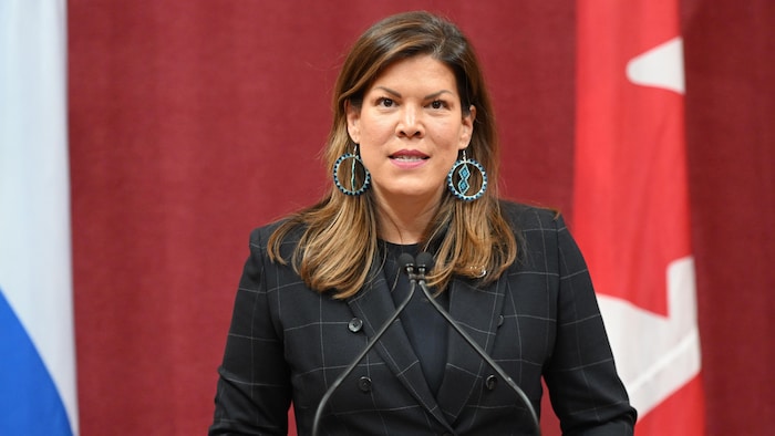 Kateri Champagne Jourdain parle dans des micros, debout derrière un lutrin, au Salon rouge de l'Assemblée nationale. 