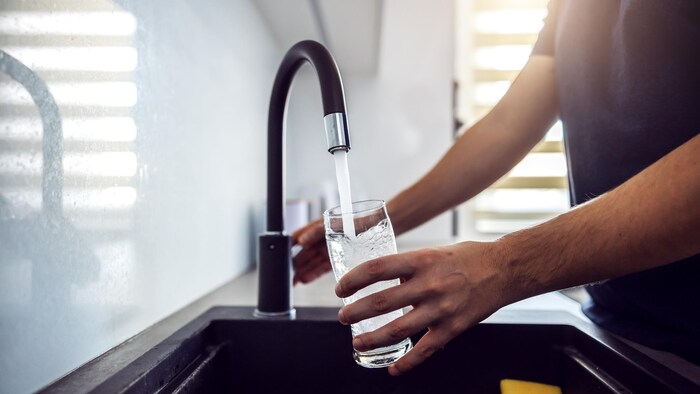 Une personne remplit un verre d'eau à un robinet.