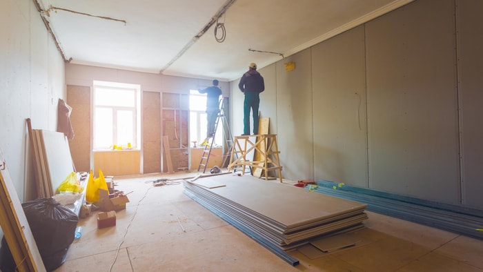 Deux personnes sont sur un escabeau et un échafaudage dans une pièce en rénovation.