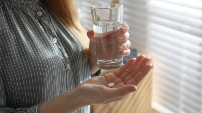 Une femme tient une pilule et un verre d'eau.