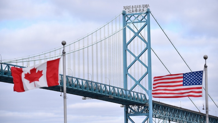 علم كندا (إلى اليسار) وعلم الولايات المتحدة يرفرفان قرب جسر ’’أمباسادور‘‘ الذي يربط مدينة ويندسور الكندية بمدينة ديترويت الأميركية والذي يُعتبر أهمّ ممرّ تجاري بين البلديْن.