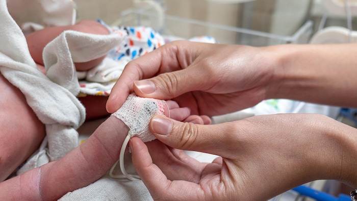 Une infirmière applique un oxymètre sur un nouveau-né. Gros plan avec mise au point sélective sur les mains. (Archives)