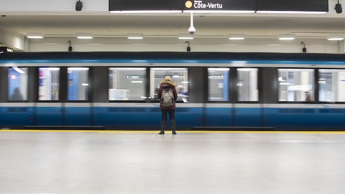 Une personne attend sur le quai de la ligne orange alors qu'une rame de métro s'immobilise sur les rails.