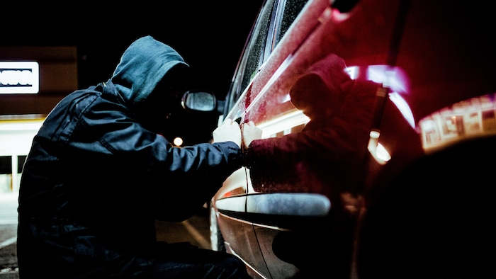 Un voleur de voiture en action tard dans la nuit, portant des vêtements noirs.