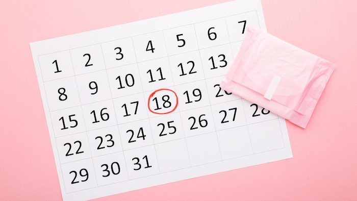 Une date est entourée dans un calendrier. Une serviette hygiénique est à côté.