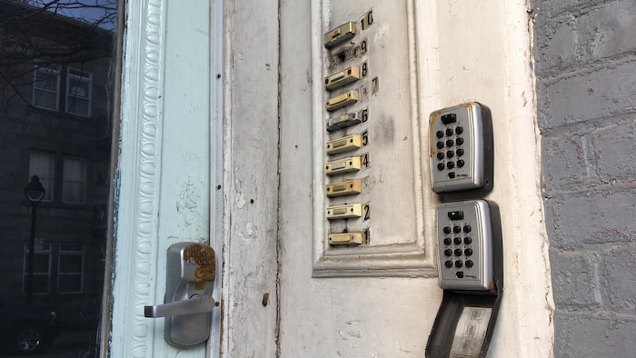 Une porte en bois sale et abîmée d'une maison de chambres de Montréal sur laquelle se trouvent 10 sonnettes.