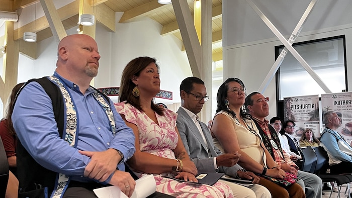 Cinq personnes assises écoutent un discours dans une salle communautaire.